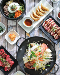 A korean food spread on a wooden table, featuring a central hot pot with noodles, vegetables, and...