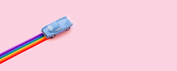Blue toy car, rainbow ribbon flag trail road, pink background. June gay parade, proud month, coming out day, human rights and tolerance concept. Minimal pop art composition. Flat lay, top view - Powered by Adobe