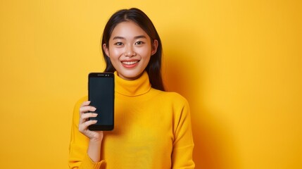 Naklejka premium She is holding a smartphone mockup with a blank screen while smiling on a yellow background.
