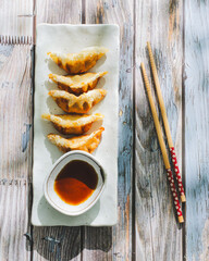 A plate of Korean fried dumplings with a side of soy sauce and a pair of chopsticks on a wooden...