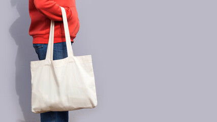 Woman in red hoodie holding tote canvas blank eco bag on street grey minimal wall background....