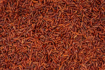 Wild raw red rice groats, food background texture, top view