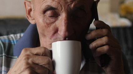 Caucasian pensioner 70 -79 years old drinking coffee from a cup and talking on the phone while inside. an elderly man has breakfast with tea and discusses problems