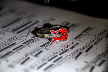 A ring in the form of a red guitar lies on the page of a book with notes.	
