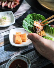 A person using chopsticks to grill various vegetables and meat on a round Korean BBQ grill at a restaurant table.