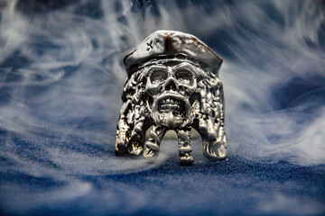A ring in the form of a pirate skull shrouded in smoke on a dark background close-up	
