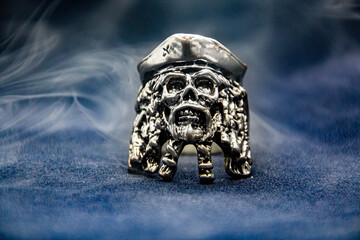 Gray smoke envelops a ring in the form of a pirate skull close-up	
