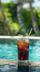 glass of iced cola with a straw, placed on the edge of a swimming pool. 