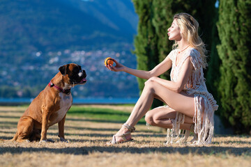 Sexy woman play with Boxer dog. Young girl throwing ball to boxer dog. Dog tries to catch ball. Sensual Woman playing with dog in park on summer day. Lovely pet. Puppy learning to obey.