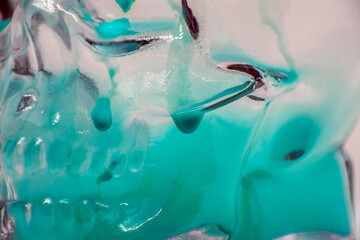 Flowing turquoise paint with drops on a transparent glass skull close-up	
