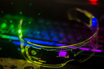 Glowing yellow futuristic glasses with transparent glass lie on a multi-colored keyboard with...