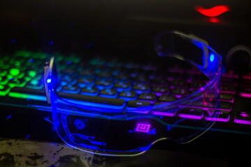 Glowing blue futuristic glasses with transparent glass lie on a multi-colored keyboard	
