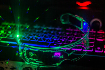 Glowing green futuristic glasses with transparent glass lie on a multi-colored keyboard with...