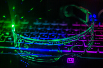 Glowing futuristic glasses with transparent glass lie on a multi-colored keyboard	
