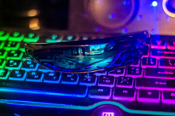Black futuristic glasses lie on a multi-colored keyboard close-up	
