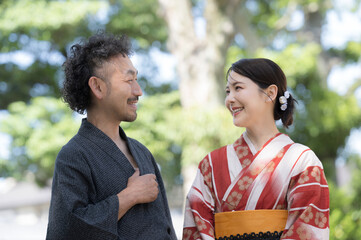 An adult Japanese couple on a date in yukata in the green outdoors, staring at each other.
