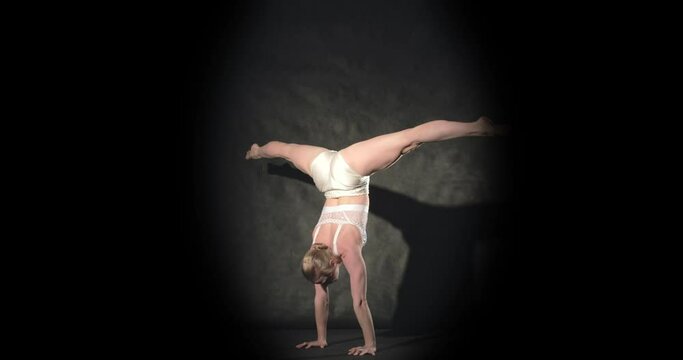 Bendy acrobat in stage spotlight does handstand with scorpion pose
