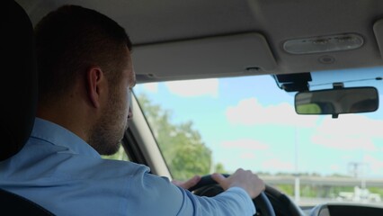 Back view of Caucasian man driving a car and looking away. Close up shot. Young adult businessman in shirt drives his car commuting to work. Business style. Successful people concept