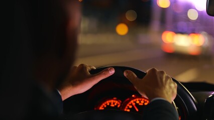 Male hands holding car steering wheel while driving. Man driving automobile at night. Close up....