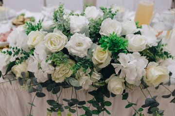 A large composition of white and yellow artificial flowers on stands against a background of white curtains