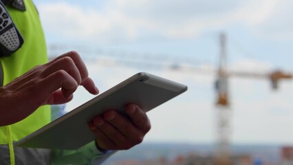 Close up of male hands holding tablet gadget tapping and scrolling on screen outdoors. Man builder engineer in uniform typing on device display with fingers, technology concept