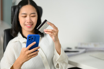 Happy young woman holding credit card making online payment or ordering via the internet on smartphone