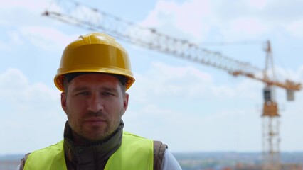 Close up of handsome happy Caucasian man builder in yellow hard hat looking at camera and smiling. Young joyful male engineer in helmet with happy face at construction site