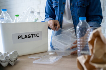 Photo of Asian woman's hands putting empty plastic bottles in the recycling bin.