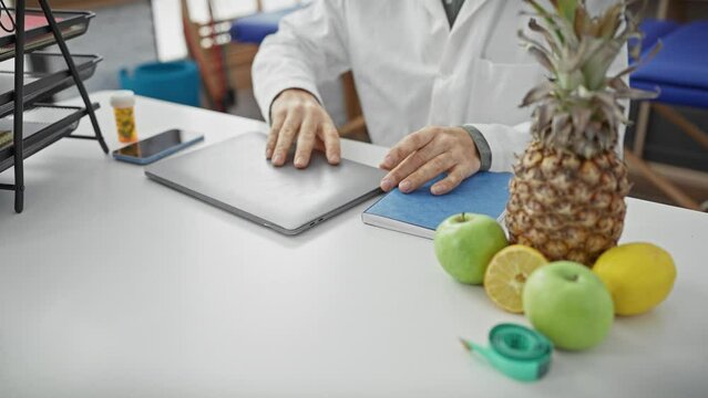 A focused man in glasses working on a laptop in a physiotherapy clinic with fruits on the desk.