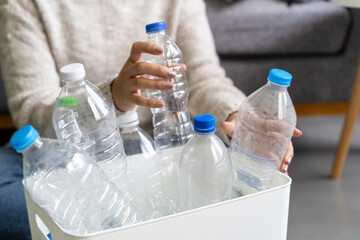 A woman wearing a cream sweater collects and sorts recycled plastic bottles into white trash cans.