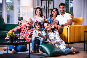 Happy Indian asian family consists of grandparents, parents and kids posing for photo sitting on sofa