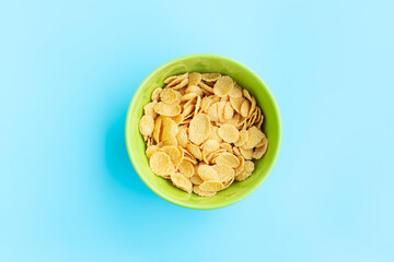 Corn flakes in green bowl on blue background, Breakfast cereal 