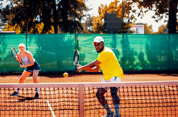 Couple playing recreational tennis on a clay court during the day.