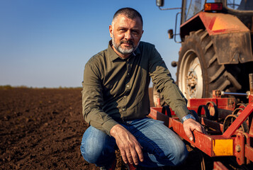 Portrait of satisfied mature farmer standing in field preparing to cultivate the land with a tractor.