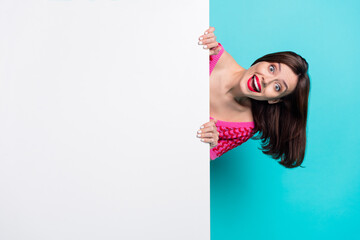 Photo of positive shocked girl appear from white billboard advertise product promotion isolated blue color background