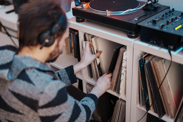 A cozy scene of a man in headphones selecting a vinyl from his music collection.