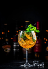 Summer refreshing cocktail drink with cognac, liqueur, sparkling wine with ice and mint in wine glass, dark background