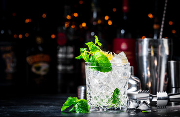 Summer refreshing drink cocktail with mint, lemon, vodka and gin tonic. Bar tools. Dark background bar counter