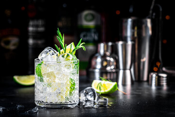 Gin tonic and rosemary cocktail drink with lime juice, sugar syrup, soda and ice. Black bar counter background