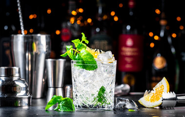 Summer refreshing drink cocktail with mint, lemon, vodka and gin tonic. Dark background bar counter