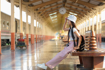 Side view of a female with a backpack sitting on the chair on the platform while waiting for the...