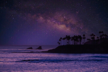Milky way above ocean in Japan, at white sand beach, and stone cliffs with small beach islands.