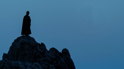 Silhouette of a Monk Standing on a Mountaintop Looking at the Sky During Dusk with Negative Space
