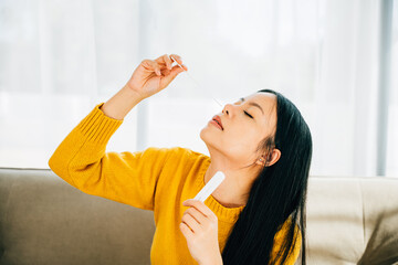 Highlighting COVID-19 self-test, Asian woman uses a rapid antigen test kit at home inserting a swab...