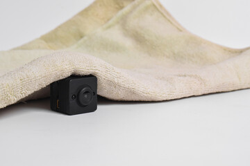 Closeup spy camera under cloth on white background. Black security camera, Mini spy camera