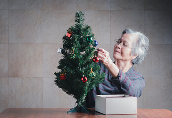 An elderly Asian woman decorating a mini Christmas tree.