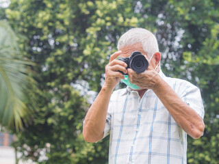 Senior man wearing a face mask taking a photo with the camera in the garden.