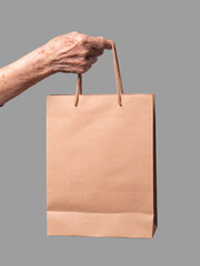 Close-up of a senior woman holding a brown paper bag against a gray background.