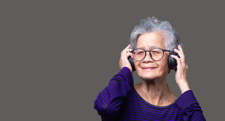 Cheerful senior woman wearing wireless headphones with a smile while standing on a gray background.