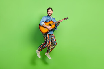 Full length photo of cheerful funky guy dressed jeans shirt jumping high enjoying guitar music...